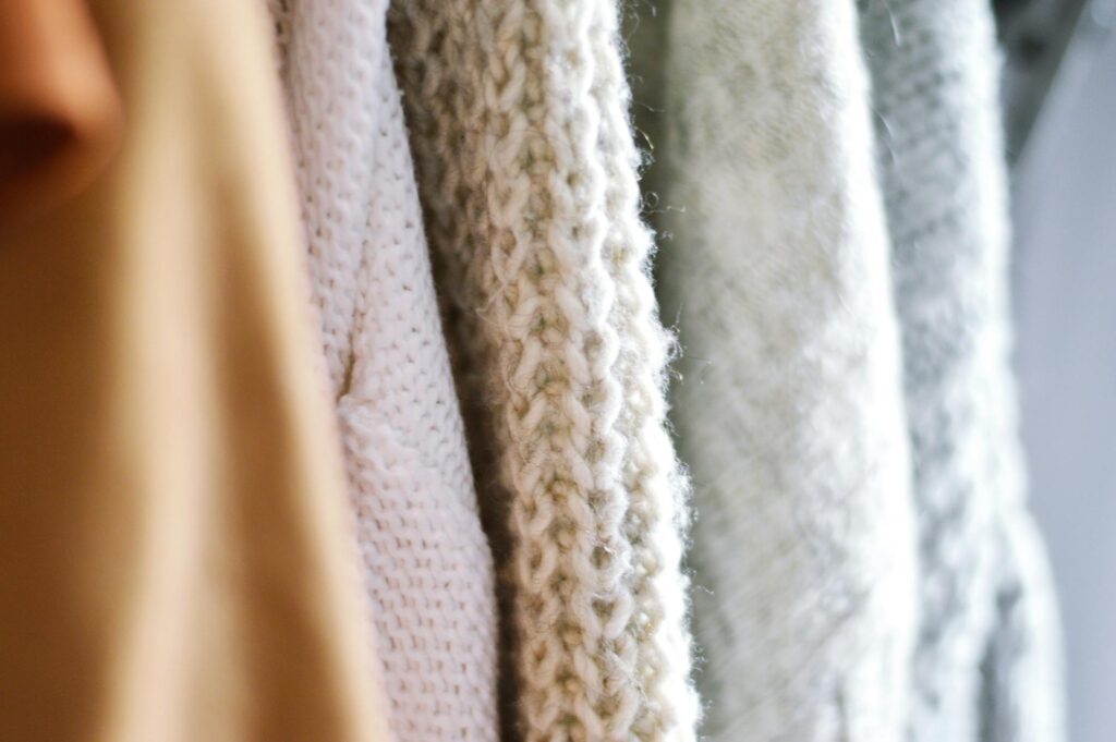 Close-up view of a warm, textured knit sweaters in soft beige and white tones, showcasing climatarian fashion fabrics with intricate weaving, knitting patterns and cozy materials.