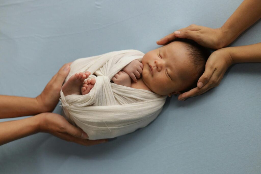Newborn wrapped in blanket, held by two adult hands—symbolizing gentle, low-waste parenting.