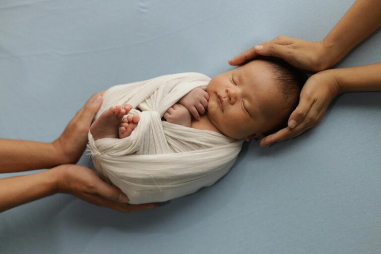 Newborn wrapped in blanket, held by two adult hands—symbolizing gentle, low-waste parenting.