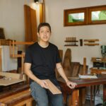 Circular furniture UK maker studio with wooden tables and chairs and an artisan sitting on one of the tables he has made.
