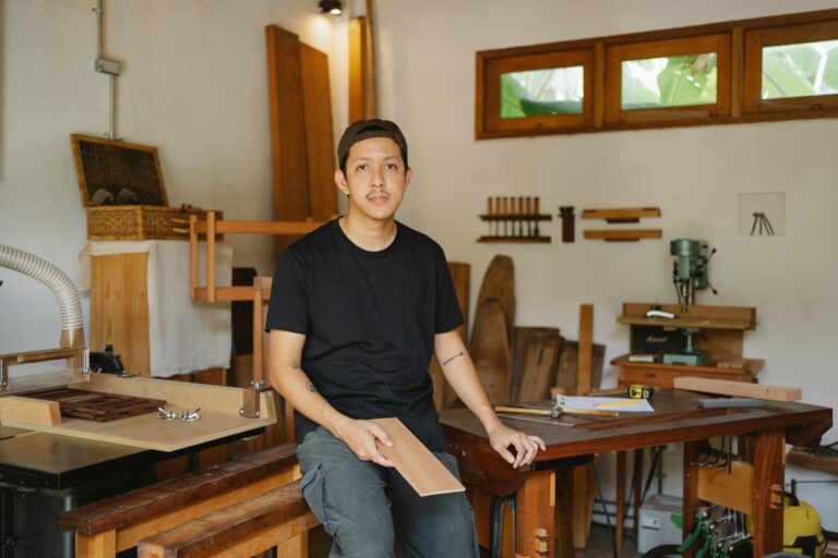 Circular furniture UK maker studio with wooden tables and chairs and an artisan sitting on one of the tables he has made.